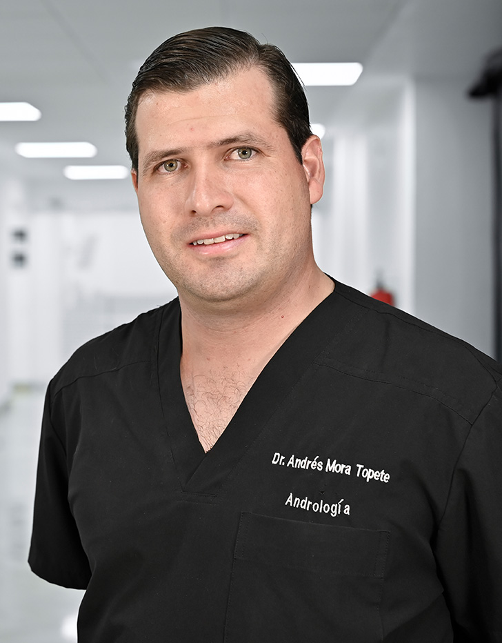 Es la foto de perfil de un médico general en Guadalajara de Hospital Angeles Del Carmen.Usa un uniforme médico color negro. Tiene poco cabello color negro. Tiene los brazos cruzados por detrás y está sonriendo ligeramente.