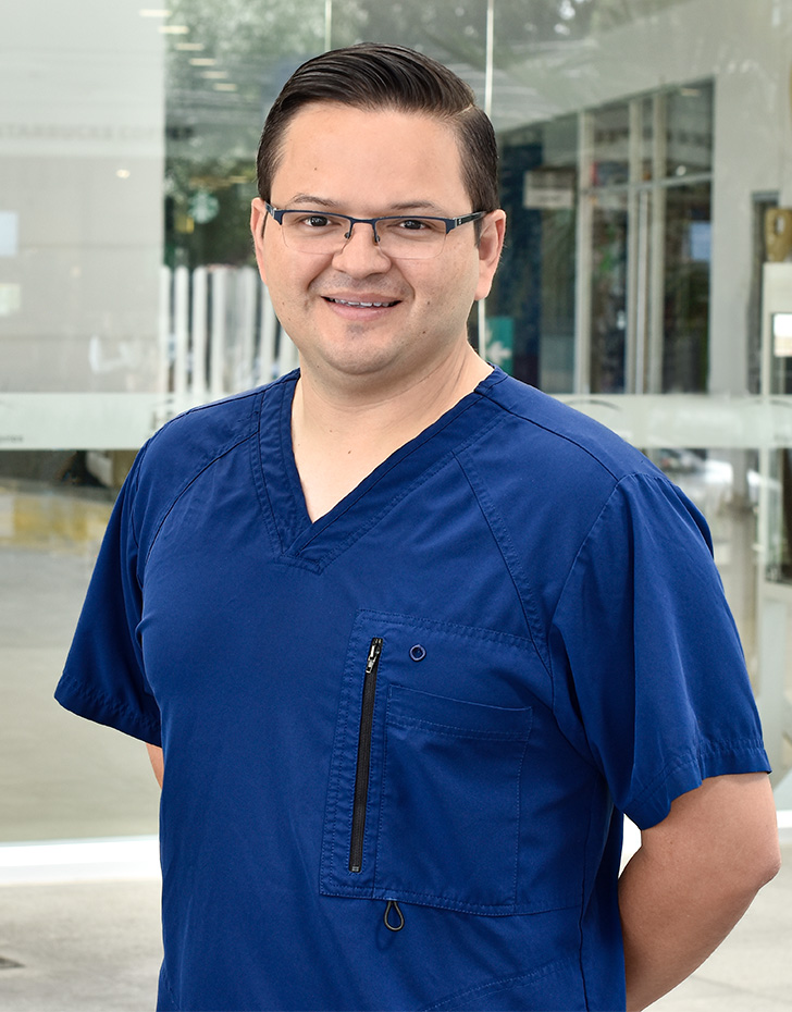 Es la foto de perfil de un neumólogo en Ciudad de México de Hospital Angeles. El doctor tiene un uniforme de color negro, tiene alrededor del cuello un estetoscopio, tiene lentes negros cuadrados y de fondo está el hospital.