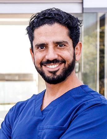 Es la foto de perfil de un cirujano general en Guadalajara de Hospital Angeles Del Carmen. Utiliza un uniforme azul, tiene barba y bigote y cabello negro.