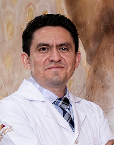 Es la foto de perfil de un psiquiatra en León de Hospital Angeles León. Utiliza una bata blanca con una camisa blanca y una corbata oscura. Tiene los brazos cruzados y está sonriendo.