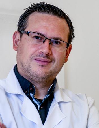 Es la foto de perfil de un pediatra en León de Hospital Angeles León. Utiliza una bata blanca con una camisa negra. Tiene lentes.
